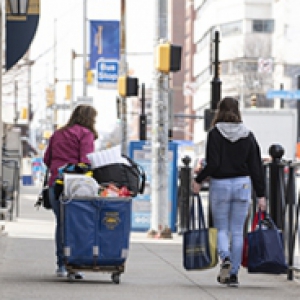 Two people walk down a sidewalk carrying luggage