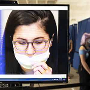 a screen showing a woman swabbing her nose, with directions in white text over a blue background that say "Hold cotton swab in place against the inside wall of your nostril for 10 seconds"