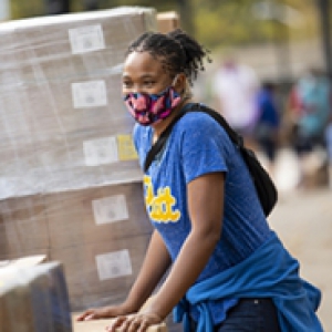A person in a face mask and blue shirt leans against a pile of boxes