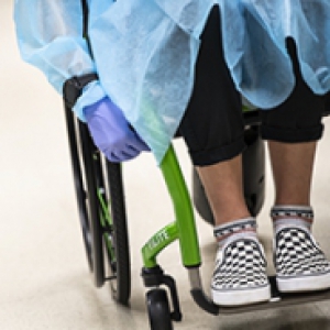 A person in a wheelchair with checkered sneakers, a blue gown and purple gloves