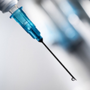 A blue-tipped syringe with a drop of liquid at the end