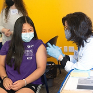 Woman applies vaccine to girl in a purple shirt