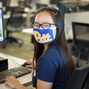 A woman in a blue Pitt face mask and shirt browses the Pitt-Greensburg website