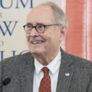 Dick Thornburgh in a gray suit and red tie shaking a man's hand behind a lectern