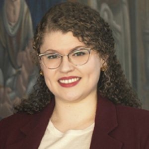 Conell in a burgundy jacket and cream-colored blouse in front of a large painting
