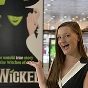 Rachel Noah in front of a banner for the play "Wicked"