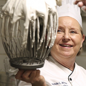 woman in a chef's hat holding up a beater covered in white cookie batter