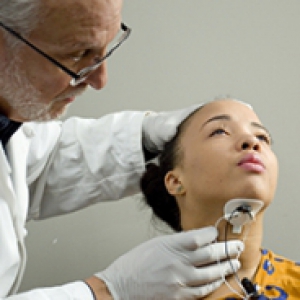 A physician in a white coat applies a device to a young woman's throat