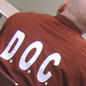 Bald man shown from the back with D.O.C. printed on his prison uniform