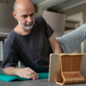 a man in a gray shirt and sweatpants exercises while watching a video on a tablet