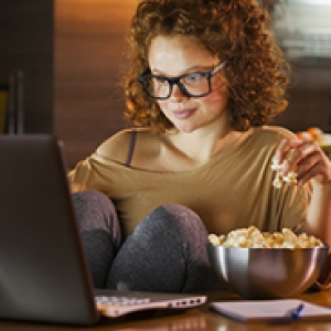 A woman eats popcorn while looking at her laptop