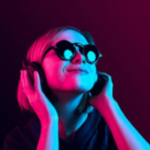 A person in sunglasses listening to music on headphones in a neon pink-blue light