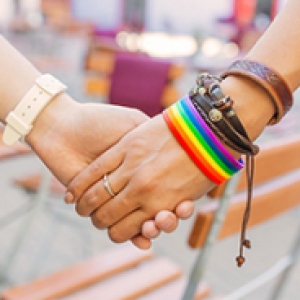a close-up of two people holding hands, one wearing a watch and the other wearing a rainbow bracelet