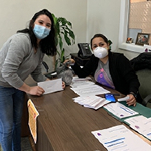 Two people in face masks, across a desk from one another
