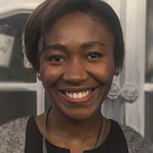 Olonisakin in a gray and black shirt, smiling