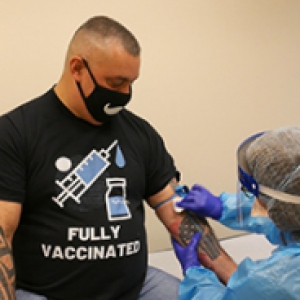 A person in a black face mask and T-shirt receiving a vaccination