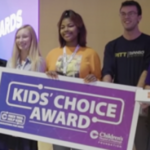three students holding a purple check-sized poster than says Kids' Choice Award
