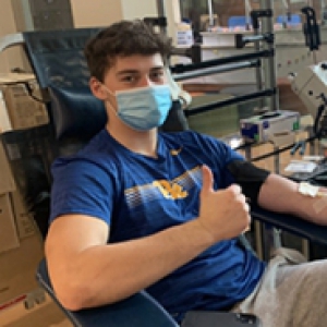 Male student athlete in a blue shirt and mask donating blood.