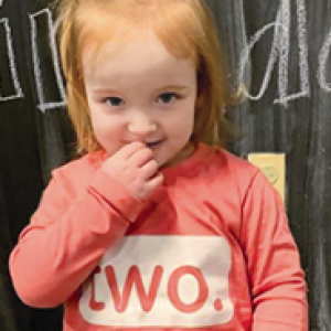a small girl in a bright pink shirt that says "two." on it