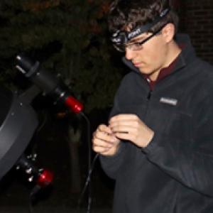 Ryan Caginalp, in a black jacket, uses a high powered telescope at night
