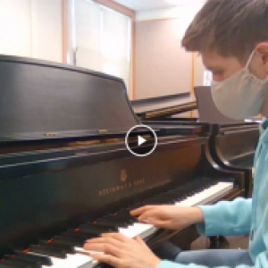 a person in a gray mask and blue sweatshirt at a piano