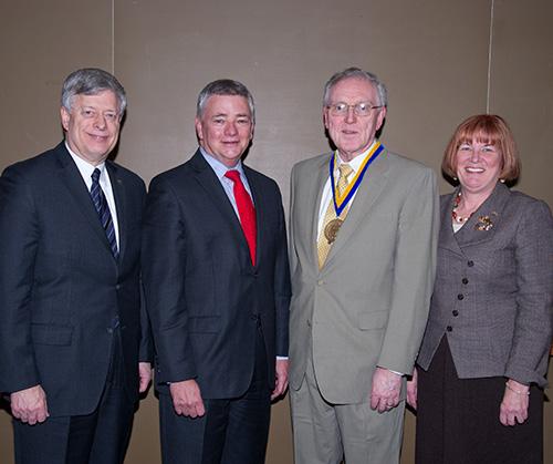 Three people stand with Maher, who wears a medal