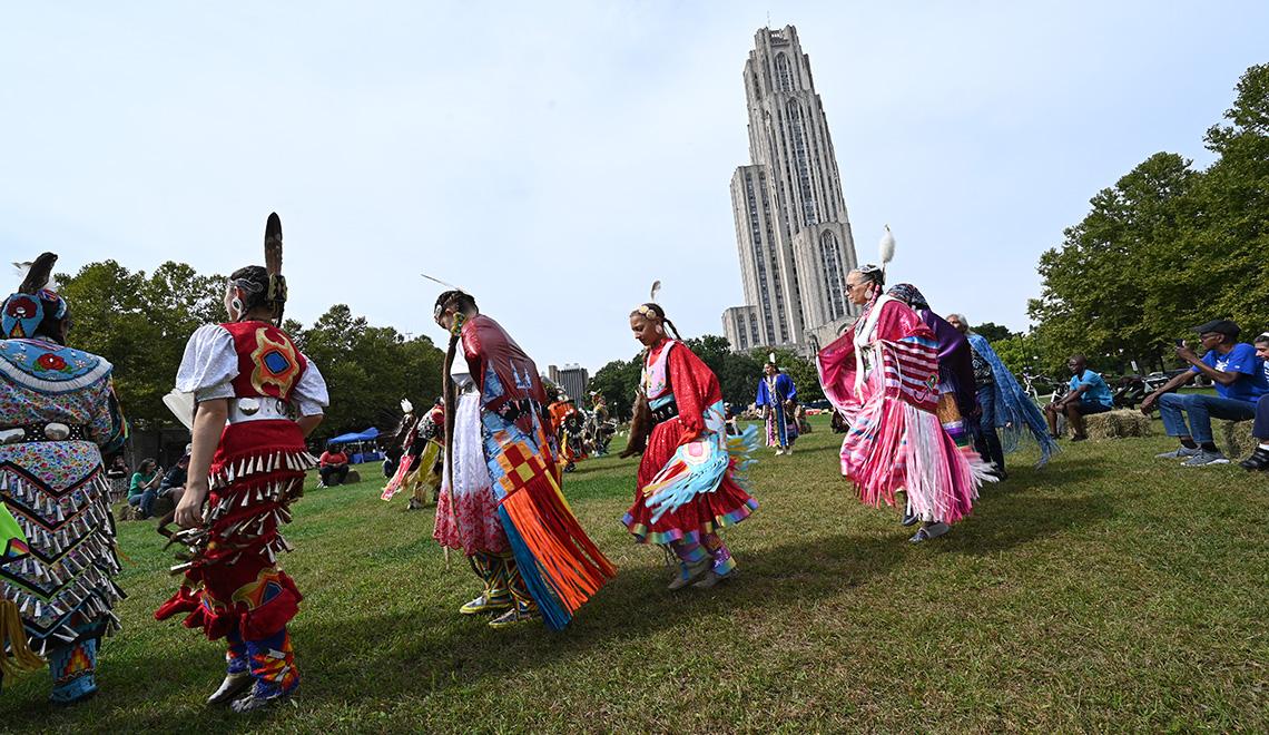 People in colorful beaded outfits dance at a powwow
