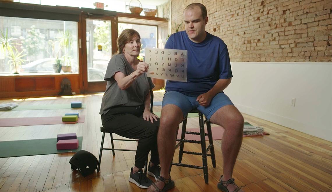 A person holds up a sheet of letters for another person to point at