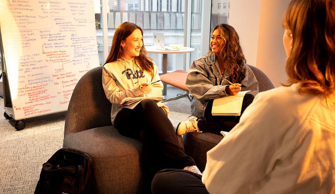 Two people laugh in front of a white board in Hillman Library