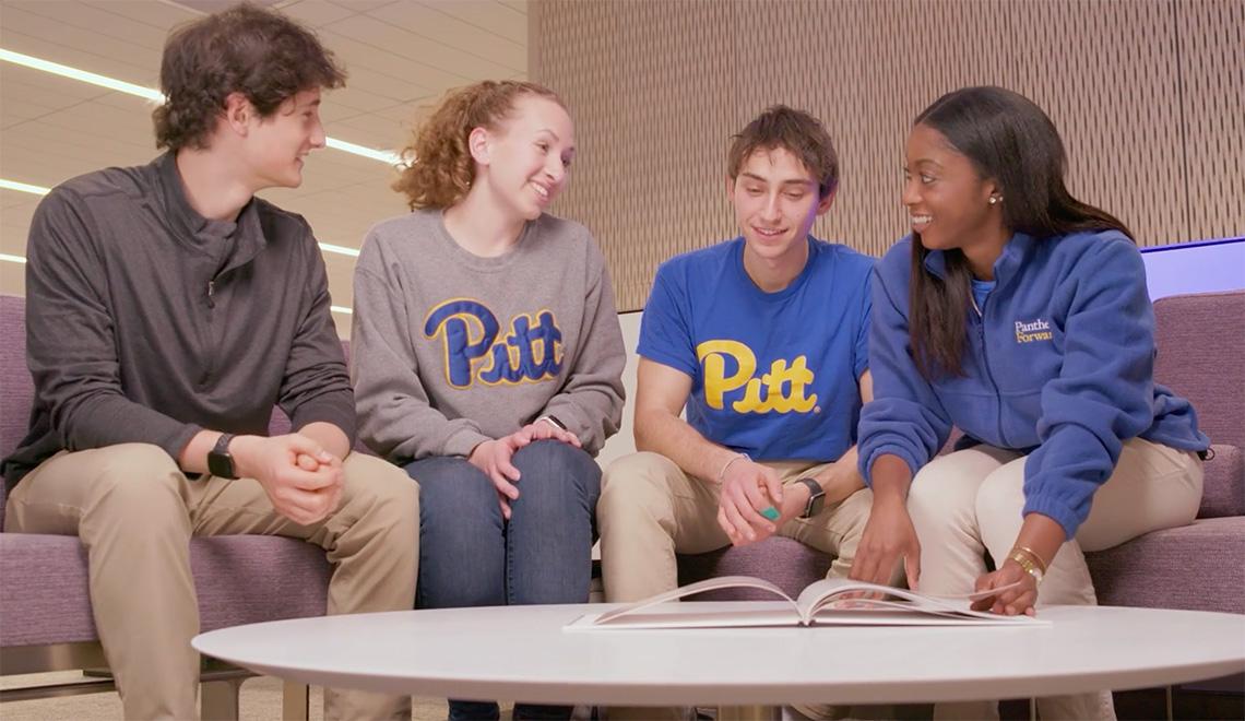 Four people gather on a couch to read a book on a coffeetable