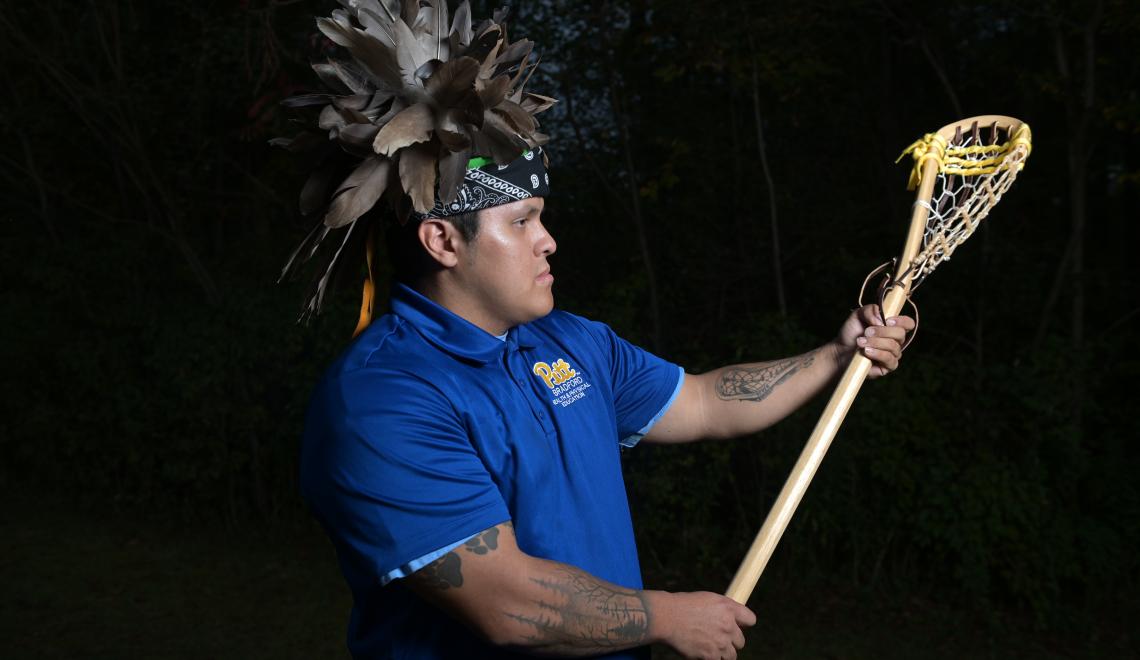 Lacrosse player posing in headdress with lacrosse stick outstretched